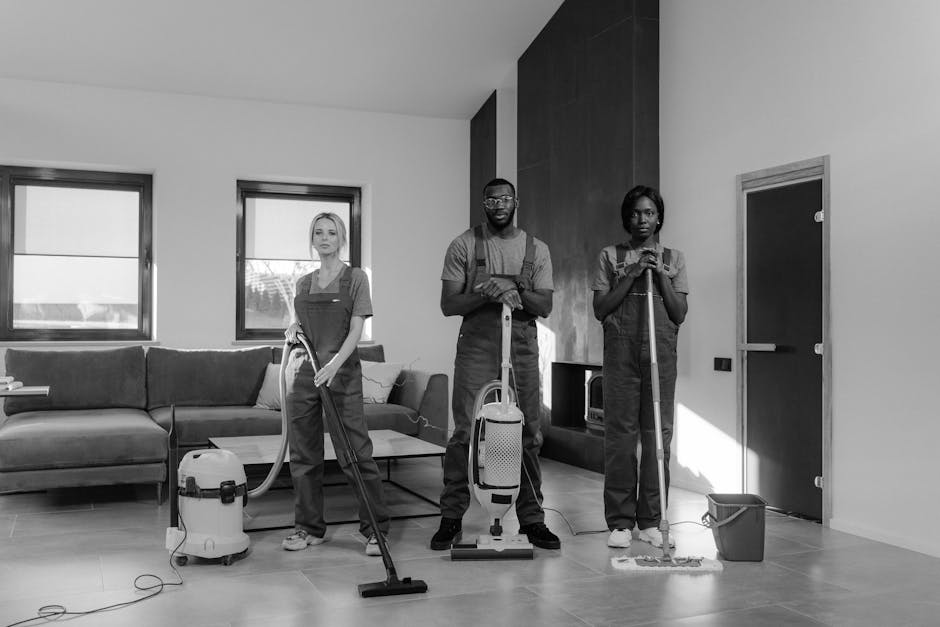 A professional cleaning team from Wembley Park Carpet Cleaners is engaged in surface cleaning and deep sanitisation of a modern living room. The room features a light-colored wooden floor, a large dar