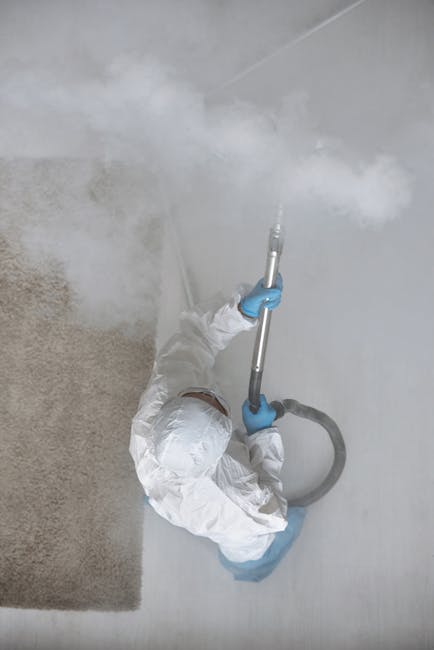 A person vacuuming a traditional patterned area rug with a yellow and black vacuum cleaner in a well-lit room. The individual is wearing beige shoes, blue jeans, and a beige coat, and is using a vacuu